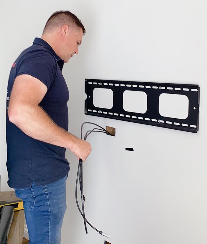 A man is putting the wires on a tv wall mount